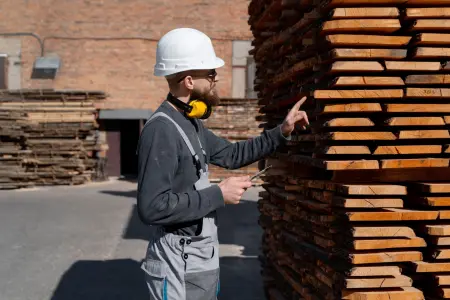 Ein Arbeiter mit Schutzhelm kontrolliert Holzbohlen in einem Lager, Baumaterial der Zukunft.